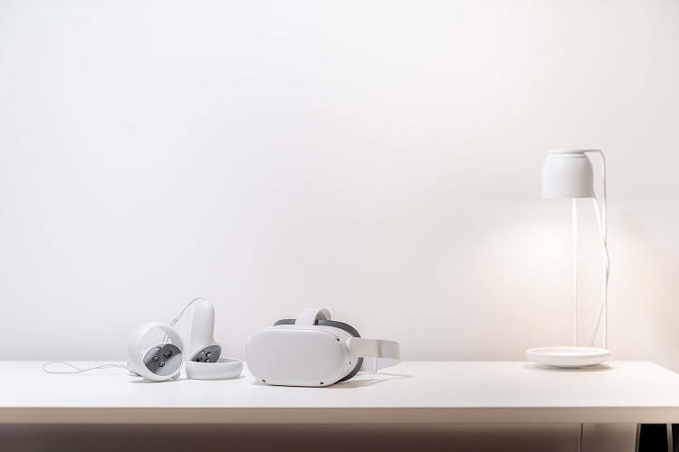 放在明亮潔白桌面上的 Meta Quest 2 VR 設備，右側有檯燈散發出柔和的光線